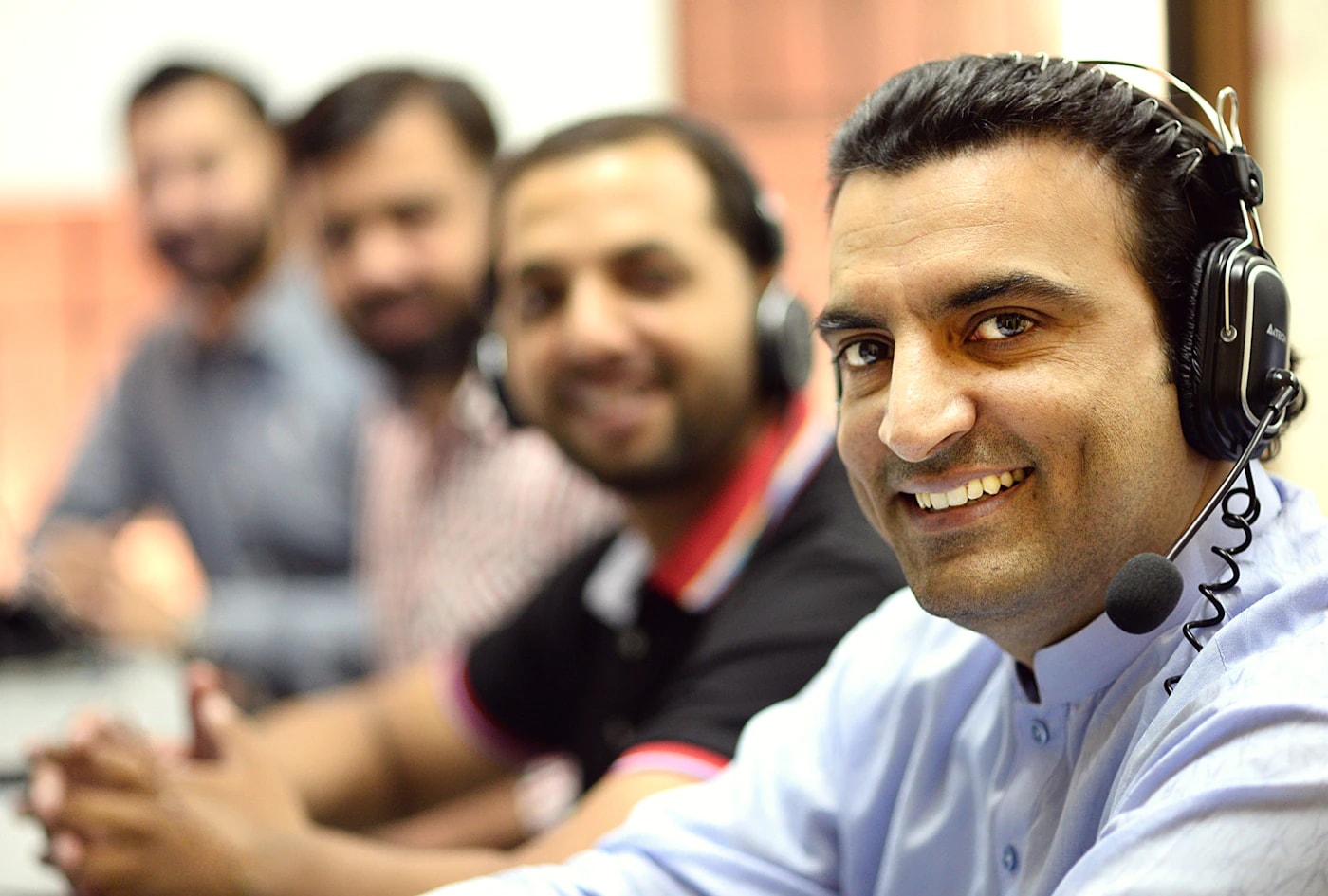 Smiling support team member wearing a headset, with colleagues working beside him